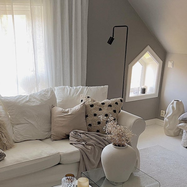 Helles Wohnzimmer mit Sofa, Kissen, Decke, Lampe und Dekorationen.