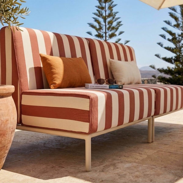 Modernes Gartensofa mit gestreifter Polsterung und Metallgestell auf einer sonnigen Steinterrasse.
