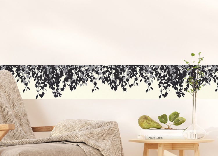 Tapetenbordüre mit hängendem Blättermotiv an einer Wand in einem hellen Zimmer mit Sessel und Beistelltisch.