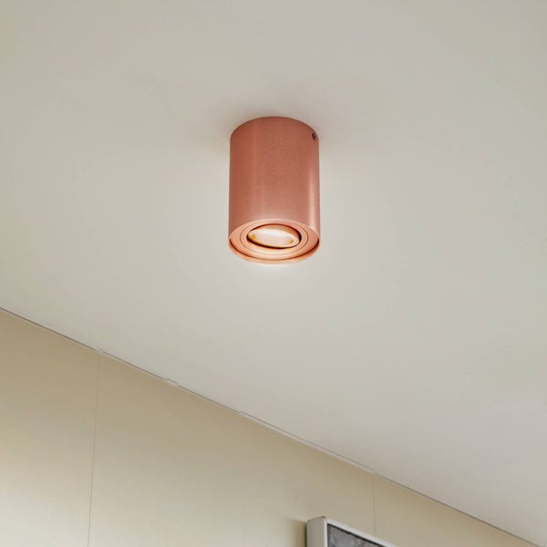 Zylindrischer Deckenstrahler in Kupferoptik an einer weißen Decke montiert mit schwenkbarem Lichtauslass.