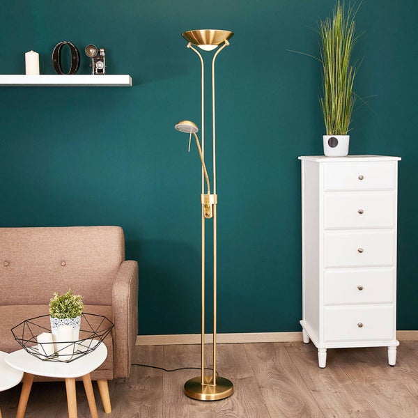 Goldfarbene Stehleuchte mit Deckenfluter und verstellbarem Lesearm in einem Wohnzimmer mit grüner Wand, Sofa und weißer Kommode.