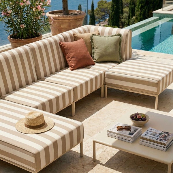 Moderne Outdoor-Lounge mit gestreiften Sitzpolstern, Dekokissen und Couchtisch auf einer hellen Terrasse am Pool.