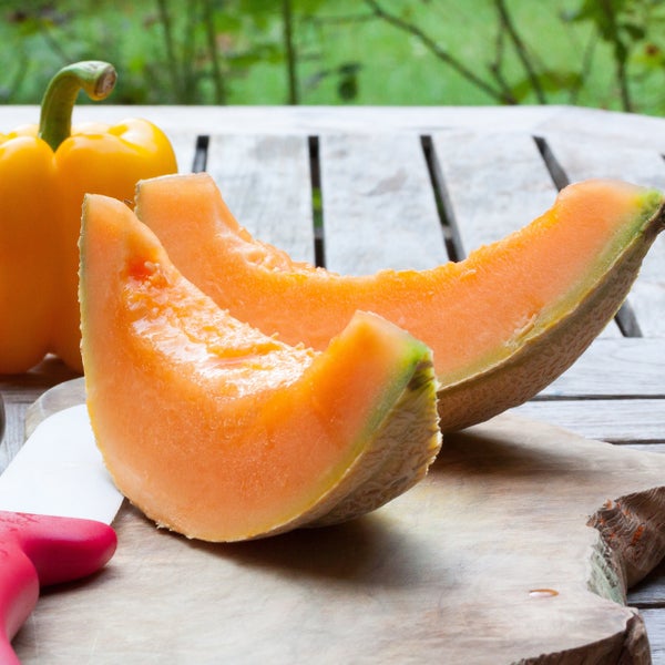 Frische Cantaloupe-Melonenscheiben und eine gelbe Paprika auf einem Holzschneidebrett im Garten.
