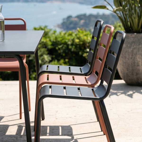 Moderne Gartenstühle aus Metall mit einer Sitzfläche aus Latten neben einem Gartentisch auf einer hellen Terrasse mit Blick auf die Küste.