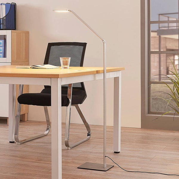 Moderne Stehleuchte aus Metall neben einem Schreibtisch mit schwarzem Bürostuhl in einem hellen Arbeitszimmer.