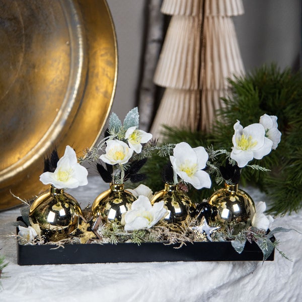 Dekorative Anordnung mit goldenen Kugeln, weißen Blumen und Tannenzweigen in einer schwarzen Schale.