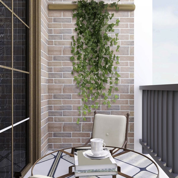 Künstlicher hängender Efeu an einer Ziegelwand auf einem hellen Balkon mit Tisch und Stuhl.