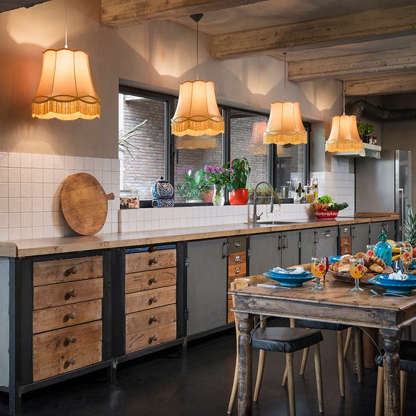 Rustikale Küche mit Industrie-Unterschränken, Pendelleuchten mit Fransen und einem gedeckten Holztisch unter einer Decke mit Holzbalken.