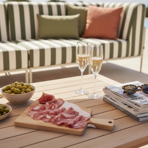 Gartenlounge mit grün-weiß gestreiftem Sofa, Holztisch, Sektgläsern, Oliven und Salami-Platte.