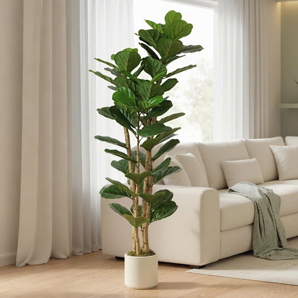 Künstliche Geigenfeige im weißen Topf in einem hellen Wohnzimmer neben einem Sofa.