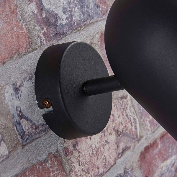 Detailansicht einer runden Wandhalterung für eine Wandleuchte aus schwarzem Metall an einer Wand in Backsteinoptik.