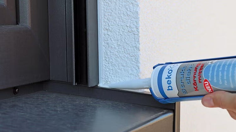 Beko Struktur-Dicht Körnungsmittel wird an einem Fensterrahmen auf einer verputzten Wand aufgetragen.