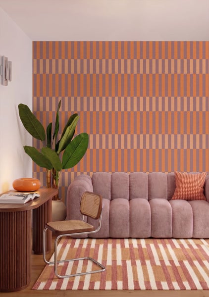 Modernes helles Wohnzimmer mit geometrisch gemusterter Tapete, rosa Polstersofa, Holzschreibtisch, Wiener Geflecht Stuhl und einer Zimmerpflanze.