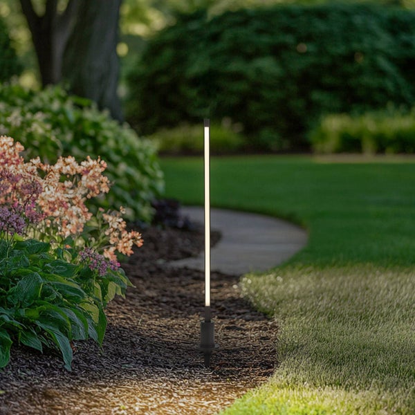 Schlanke schwarze LED-Gartenleuchte beleuchtet einen Gartenweg mit Mulchbeet, Rasen und blühenden Pflanzen.