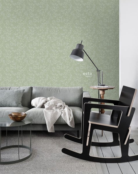 Wohnzimmer mit grauer Couch, Couchtisch und Schaukelstuhl vor einer Wand mit Blattmuster-Tapete