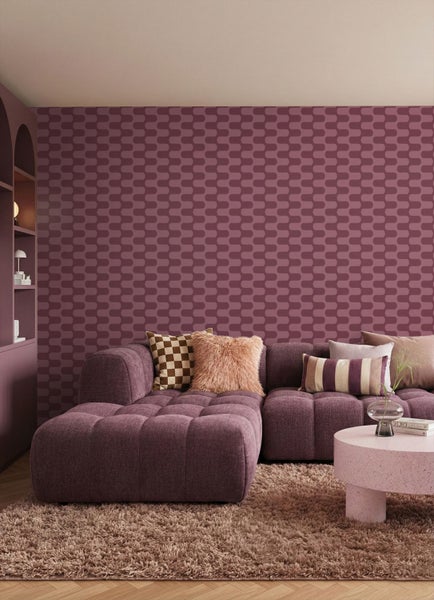 Wohnzimmer mit gemusterter Vliestapete in Beerentönen, passendes Ecksofa, runder Couchtisch und heller Hochflorteppich.