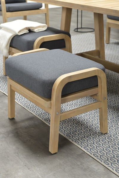 Gartenhocker aus hellem Holz mit dunkelgrauem Sitzpolster in einer hellen und organisierten Sitzgruppe auf einem gemusterten Teppich.