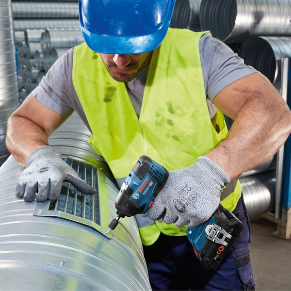Ein Handwerker befestigt mit einem Akku-Schlagschrauber ein Lüftungsgitter an einem Rohr.