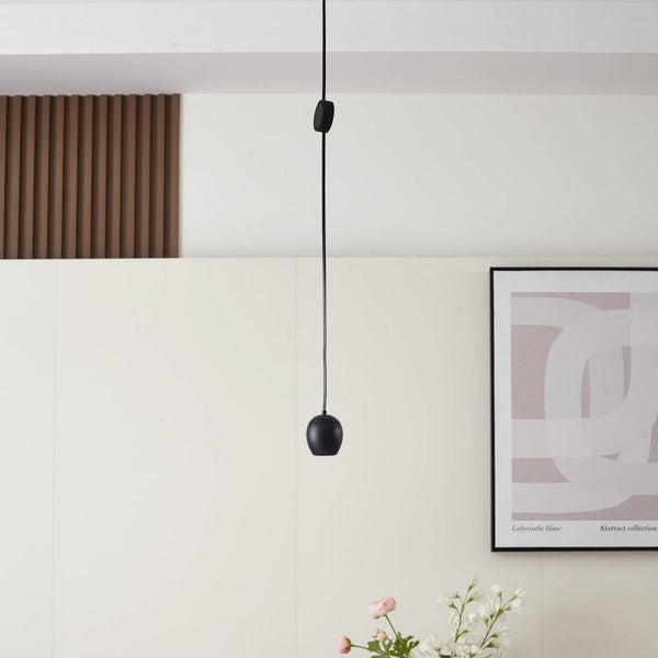 Schwarze Pendelleuchte in minimalistischem Design in einem hellen Wohnraum mit Holzlamellen und Wandbild.