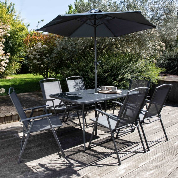 Gartenmoebel-Set mit rechteckigem Glastisch, sechs Klappstuehlen aus Metall und Textilgewebe sowie einem Sonnenschirm auf einer Holzterrasse.