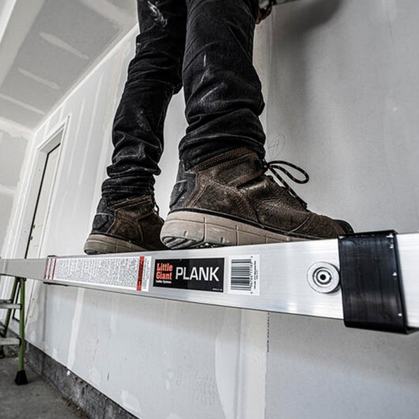 Eine Person steht auf einem Little Giant Arbeitsgerüstbrett aus Aluminium, das zur Deckenmontage vor einer Gipskartonwand verwendet wird.