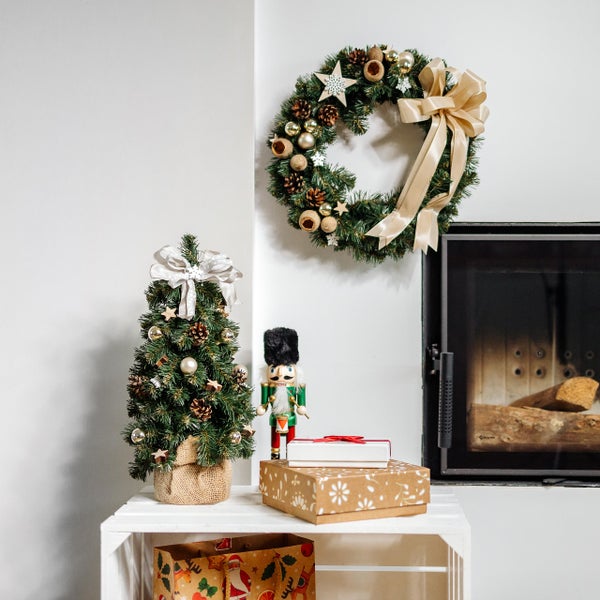 Festlicher Adventskranz aus grünen Tannenzweigen mit Zapfen, Kugeln und einer brennenden weißen Kerze auf einem Holztisch.