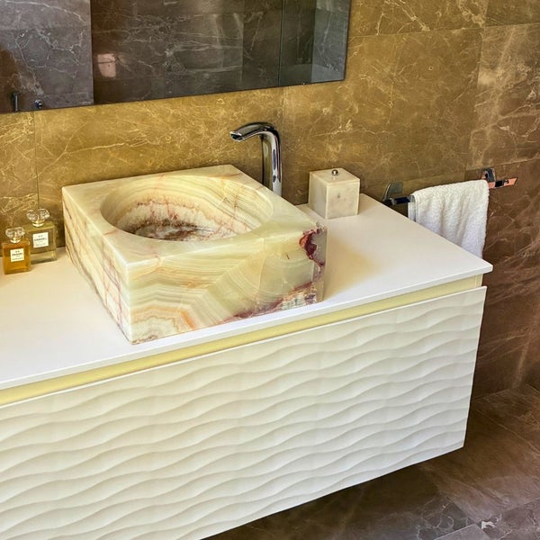 Modernes Badezimmer mit einem Natursteinwaschbecken auf einem weißen Unterschrank mit Wellenstruktur und verchromter Armatur.