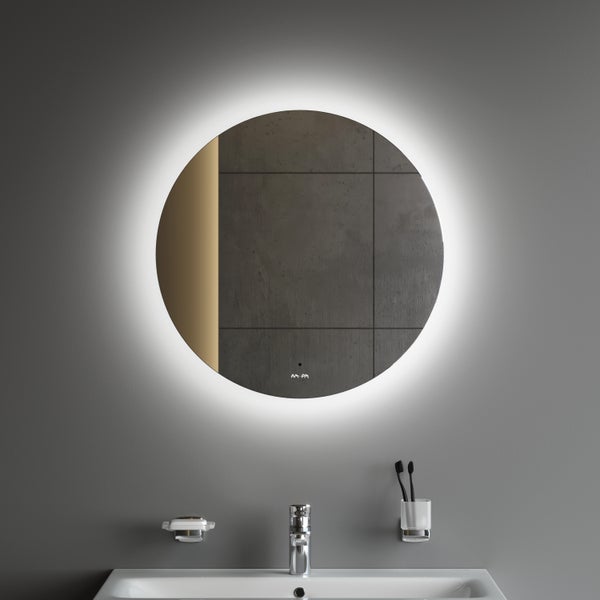 Runder Badezimmerspiegel mit Hintergrundbeleuchtung über einem Waschbecken mit verchromter Armatur und Badzubehör in einem hellen Badezimmer.