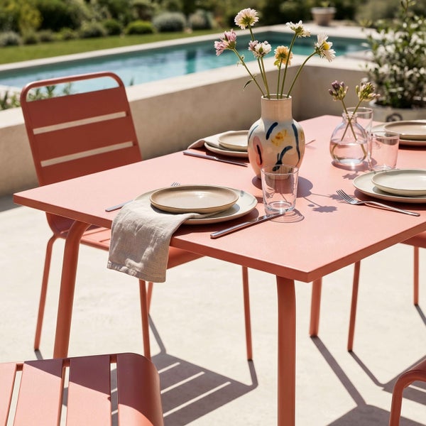 Moderner Gartentisch und passende Metallstühle auf einer sonnigen Terrasse am Pool, gedeckt mit Tellern, Gläsern und Blumenvasen.