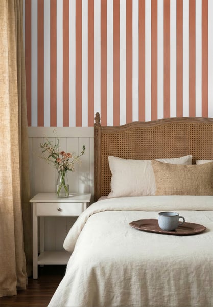 Hell eingerichtetes Schlafzimmer mit gestreifter Vliestapete, weißer Wandvertäfelung und einem Bett mit Rattankopfteil.
