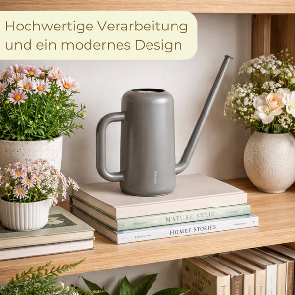 Moderne Zimmergießkanne in Anthrazit mit langem Ausguss auf einem Holzregal neben Blumen in Töpfen und Büchern in einer hellen Umgebung.