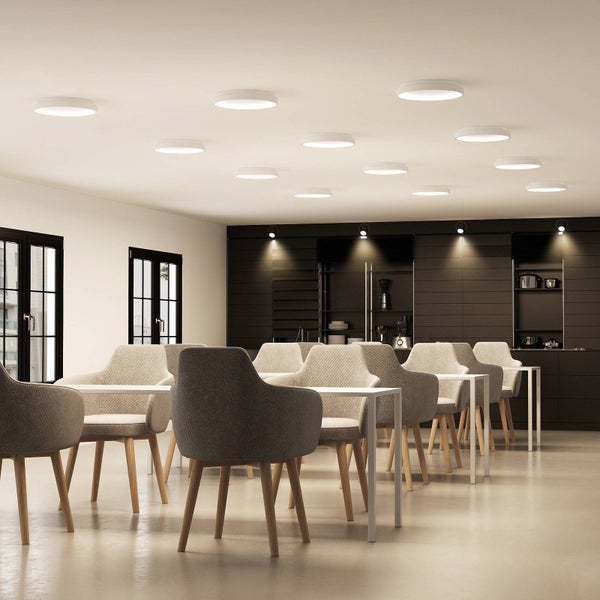 Moderner heller Raum mit runden LED-Deckenleuchten, weißen Tischen und grauen Polsterstühlen mit Holzbeinen.