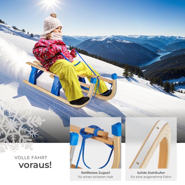 Kind fährt mit einem Holzschlitten mit Zugseil und Stahlkufen einen schneebedeckten Hang hinunter.