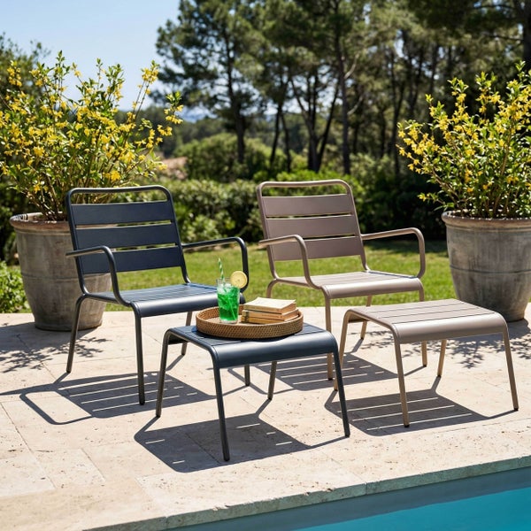 Zwei Loungesessel aus Metall mit passenden Hockern auf einer sonnigen Terrasse am Pool, umgeben von Pflanzen.