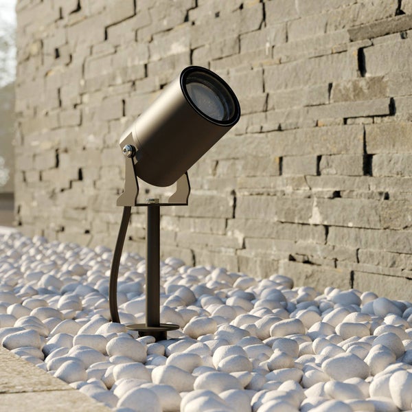 Dunkelgrauer Außenstrahler mit Erdspieß in weißen Steinen vor einer Natursteinmauer.