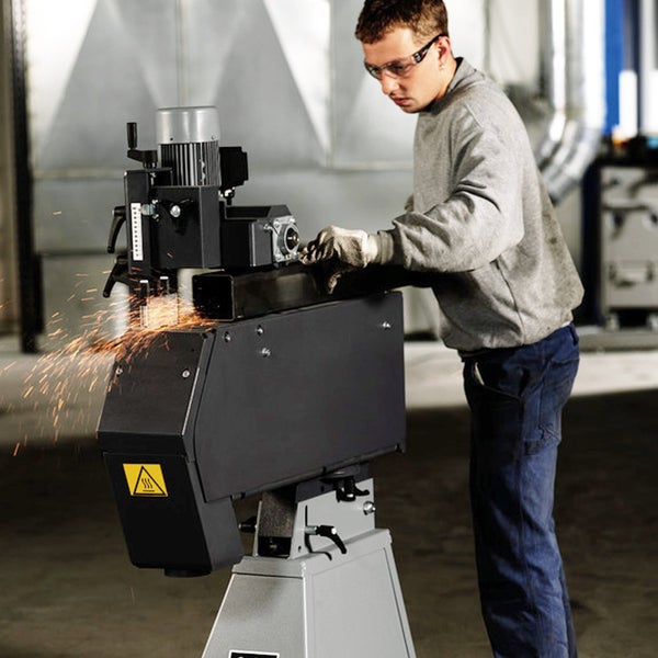 Handwerker bedient eine industrielle Metallschleifmaschine in einer hellen Werkstatt, beim Schleifen eines Metallrohrs entstehen helle Funken.