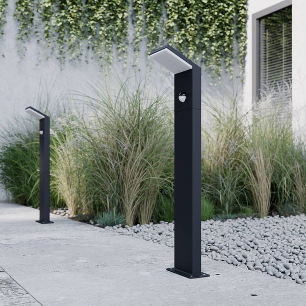 Moderne schwarze LED-Wegeleuchten mit Bewegungsmelder an einem Gartenweg mit Gräsern und Kieselsteinen.