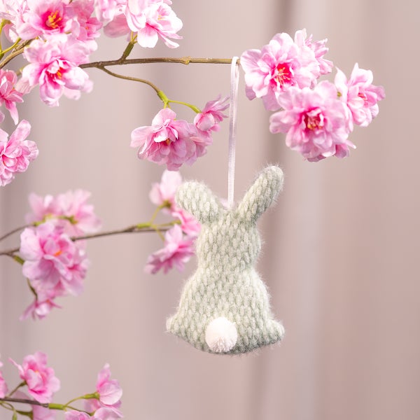 Dekorativer Strickhase mit Band zum Aufhängen an einem blühenden Zweig