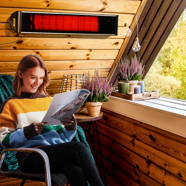 Gemütliche Leseecke auf einer Holzterrasse mit Heizstrahler und dekorativen Elementen wie Heidekraut und Lichterketten.