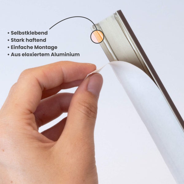 Hand zieht die Schutzfolie von einer selbstklebenden Profilleiste aus eloxiertem Aluminium ab.