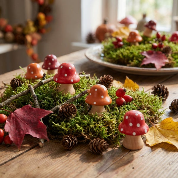 Herbstliche Tischdekoration mit kleinen Holzpilzen, Moos, Kiefernzapfen, Hagebutten und Ahornblättern auf einem Holztisch.