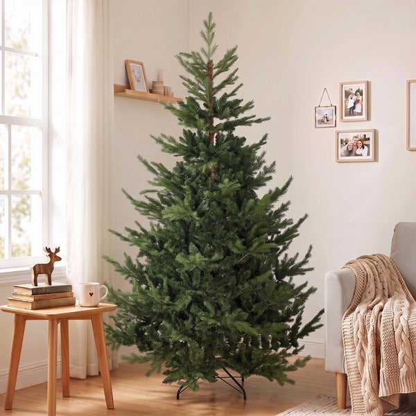 Ein künstlicher Weihnachtsbaum steht in einem hellen, wohnlich eingerichteten Wohnzimmer neben einem Beistelltisch mit Dekoration.