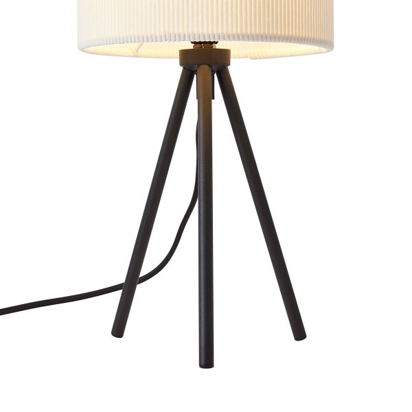 Tischleuchte mit modernem Dreibein-Metallgestell in Schwarz und weißem, geripptem Stoffschirm.