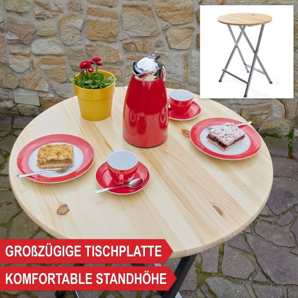 Runder Stehtisch aus Holz mit klappbarem Metallgestell, gedeckt mit Kaffeegeschirr und Thermoskanne im Außenbereich vor einer Steinmauer.
