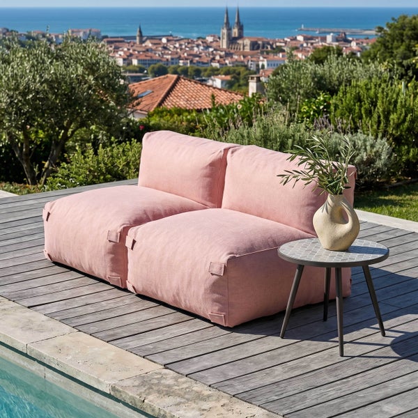 Zweisitziges Outdoor-Sitzsack-Sofa in Rosa auf einer Holzterrasse am Pool mit Beistelltisch und Blick auf eine Küstenstadt.