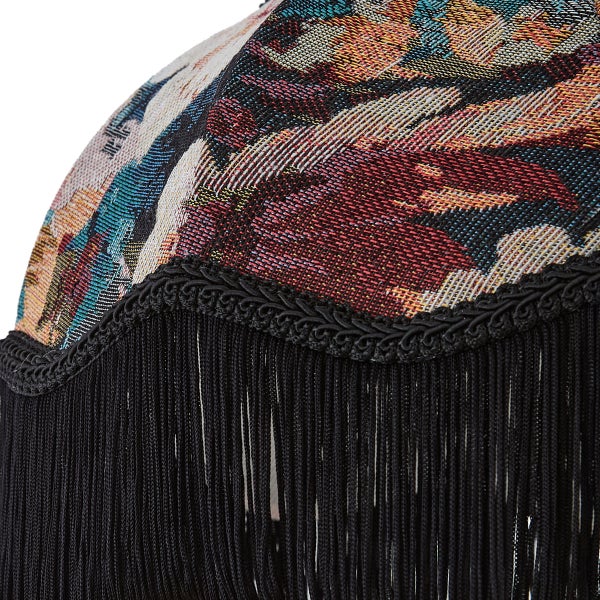 Nahaufnahme eines Lampenschirms aus gemustertem Stoff mit schwarzen Fransen und einer geflochtenen Borte.