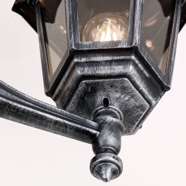 Detailaufnahme einer Außenwandleuchte im Laternen-Stil aus Metall mit Glaseinsätzen und sichtbarem Leuchtmittel.