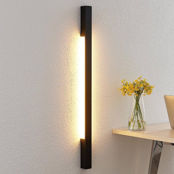Moderne schwarze LED-Wandleuchte in langer, schmaler Form an einer Wand neben einem Schreibtisch mit gelben Blumen.