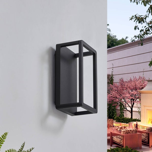 Moderne rechteckige Außenwandleuchte in Schwarz an einer Wand, im Hintergrund eine Terrasse mit Kamin und Garten.