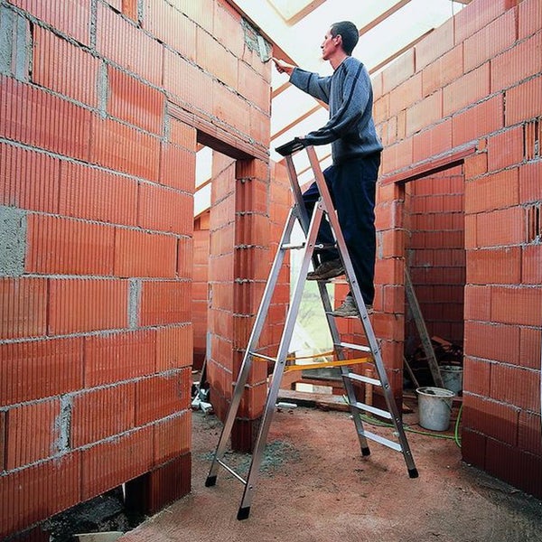 Mann auf einer Leiter bei Maurerarbeiten an einem Haus aus Ziegelsteinen